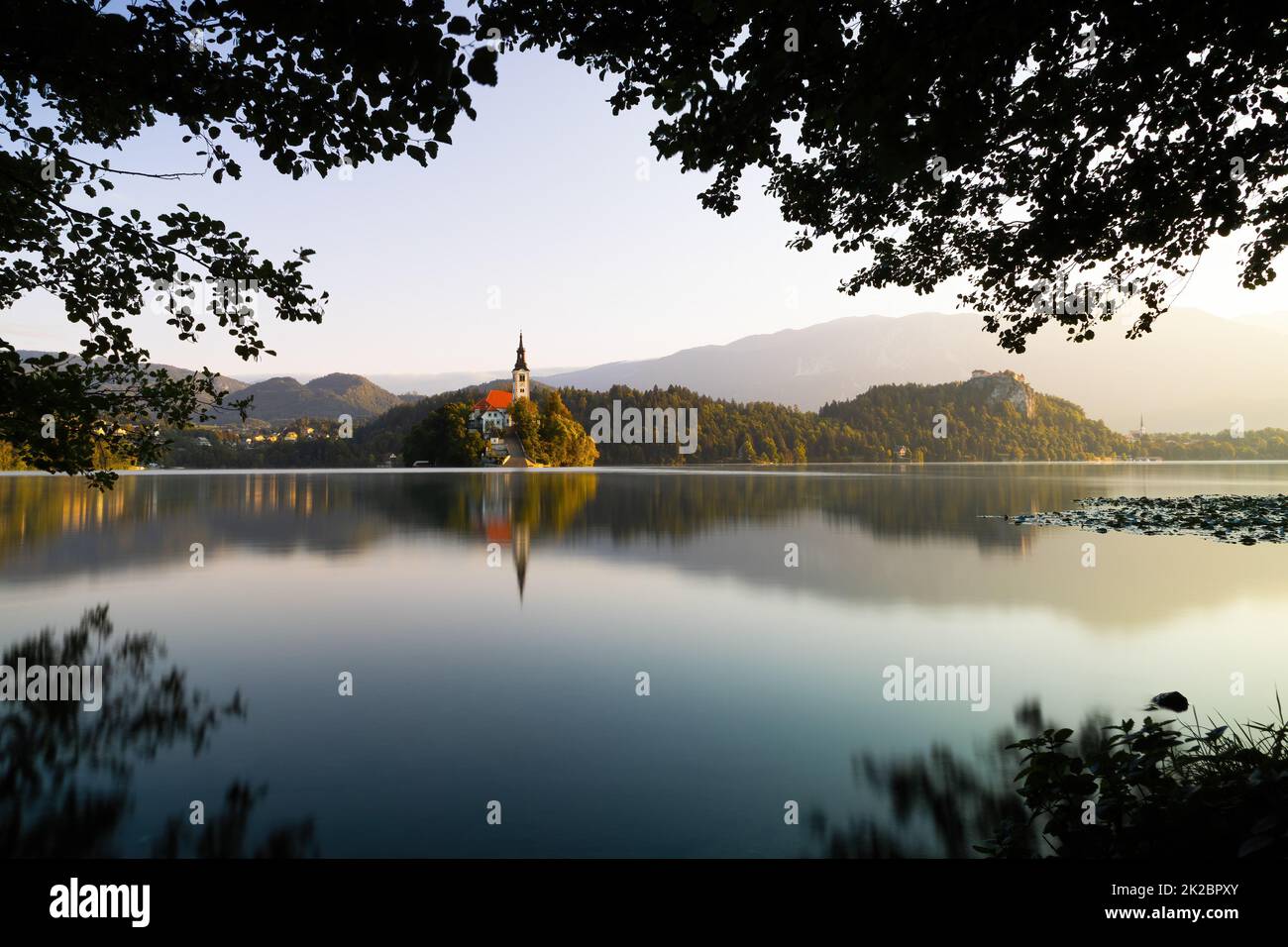 Lake Bled with a church on an island at sunrise through window of branches Stock Photo