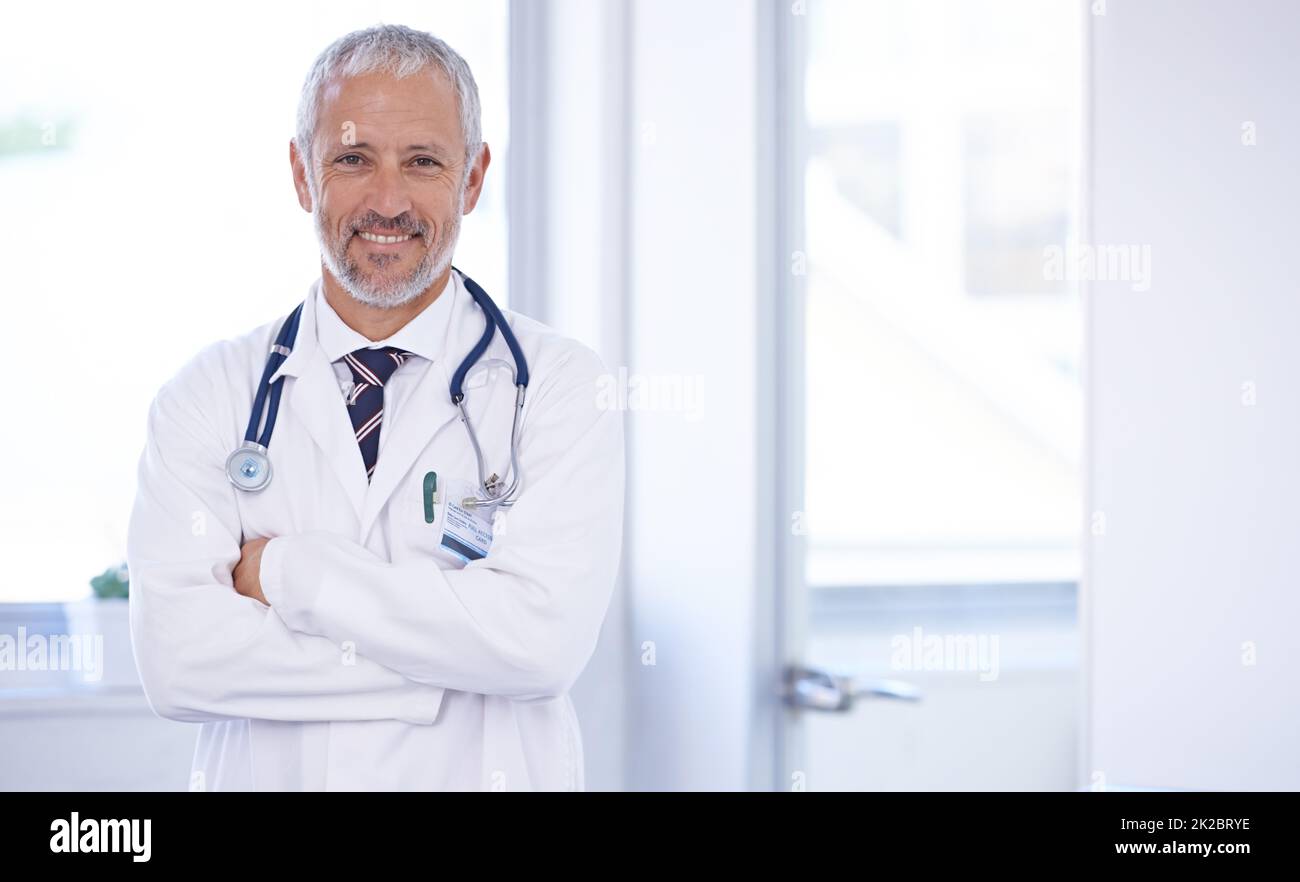 The trusted family doctor. Portrait of a doctor standing in a well-lit room with his arms crossed. Stock Photo