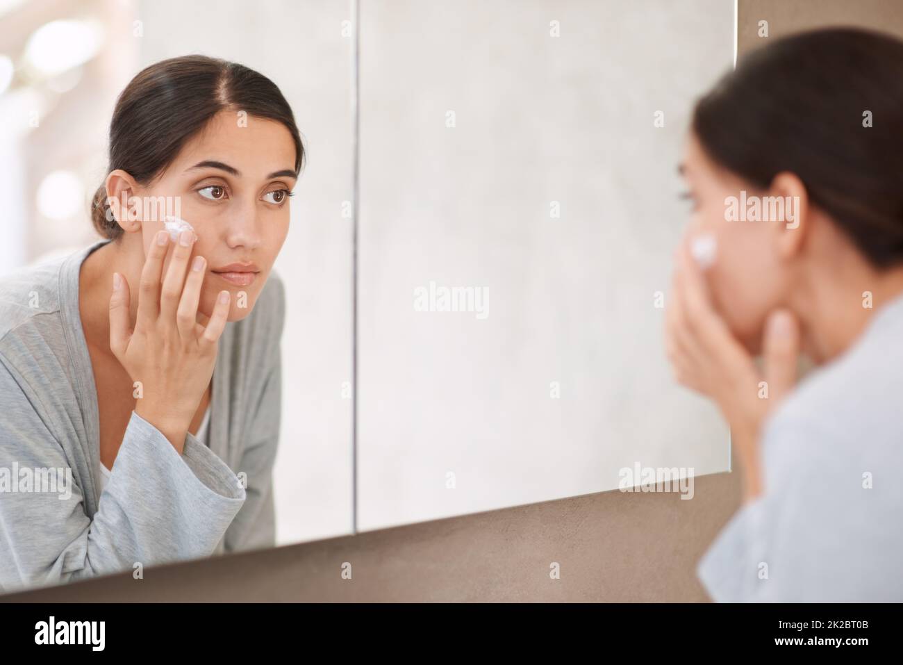 Taking good care of her skin. Shot of a beautiful woman applying moisturizer to her face. Stock Photo