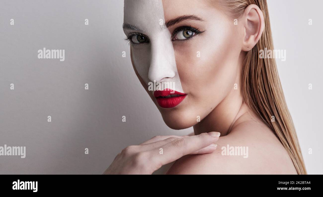 Living in a world of red and white. Shot of a beautiful woman wearing face paint and red lipstick against a plain background. Stock Photo