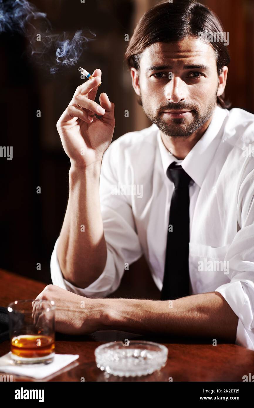 Classy and filled with confidence. Portrait of a well-dressed young man sitting at a bar with a drink. Stock Photo