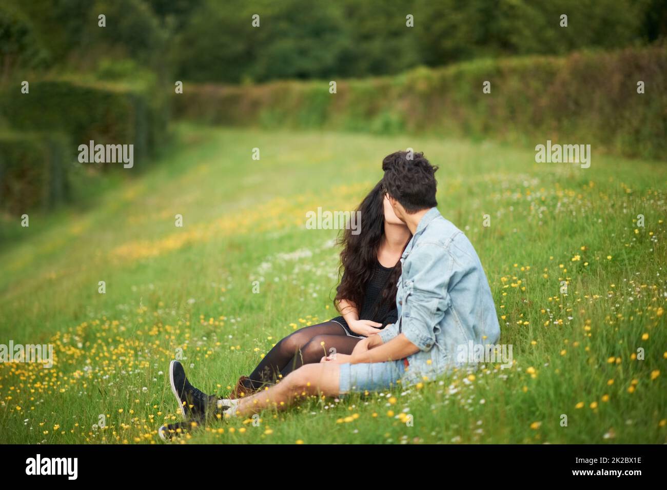 Springtime romance. Cute young couple sitting in a springtime field kissing. Stock Photo