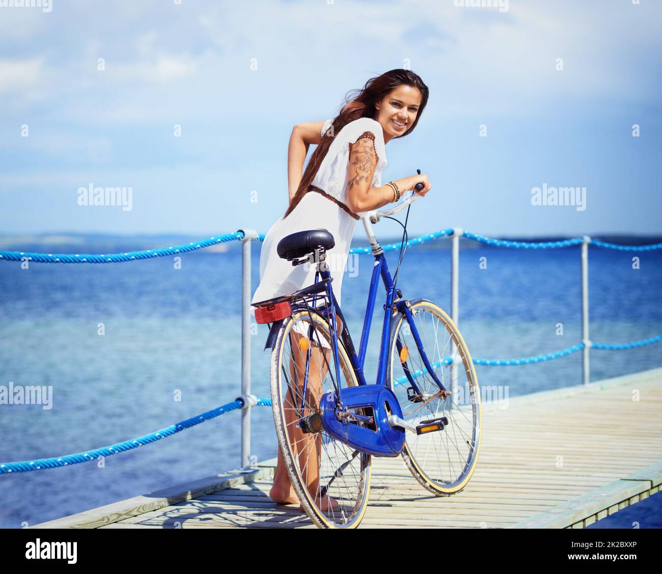 Bicycle fun beside the sea. Full length shot of a gorgeous tattooed young woman pushing her bicycle along a pier. Stock Photo