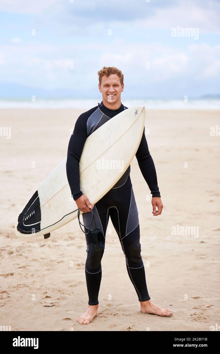 Up for surfing. A young man holding his surfboard at the beach Stock