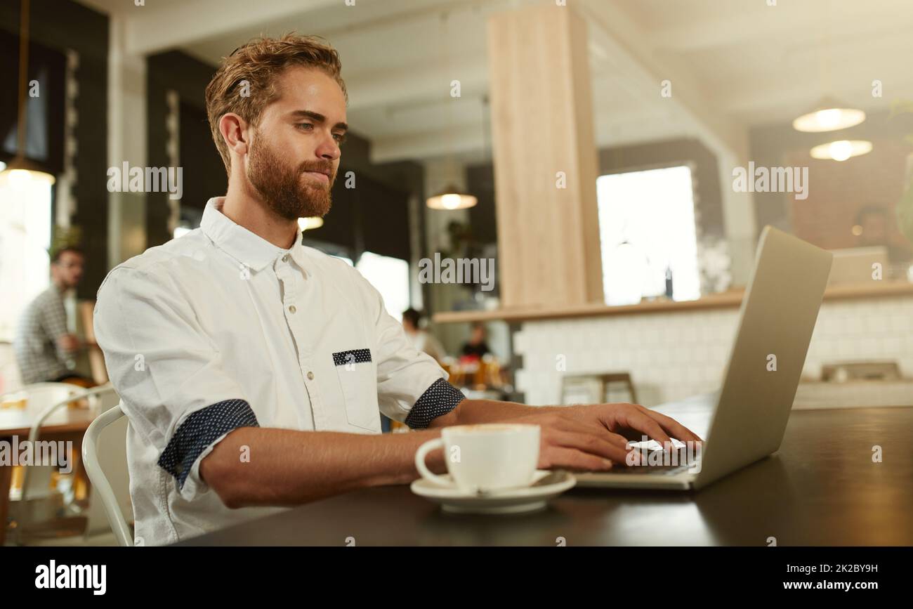 His perfect working environment. Shot of a young man using a laptop in a cafe. Stock Photo