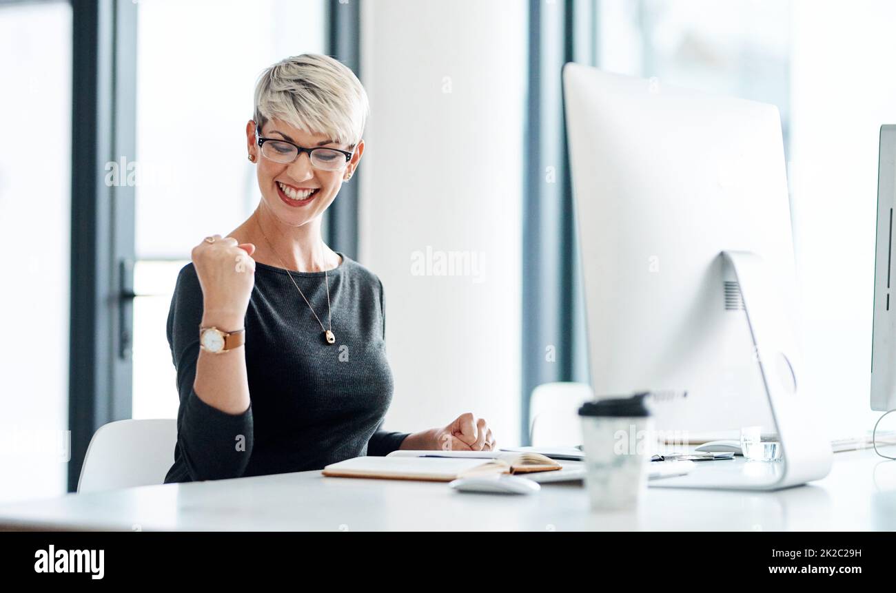 Winning isnt everything, its the only thing. Shot of a young businesswoman cheering while working on a computer in an office. Stock Photo