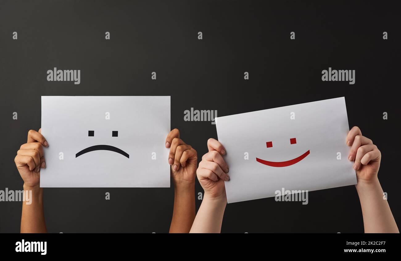 Happy and sad. Shot of two people holding a sign with happy and sad smileys on against a dark background. Stock Photo