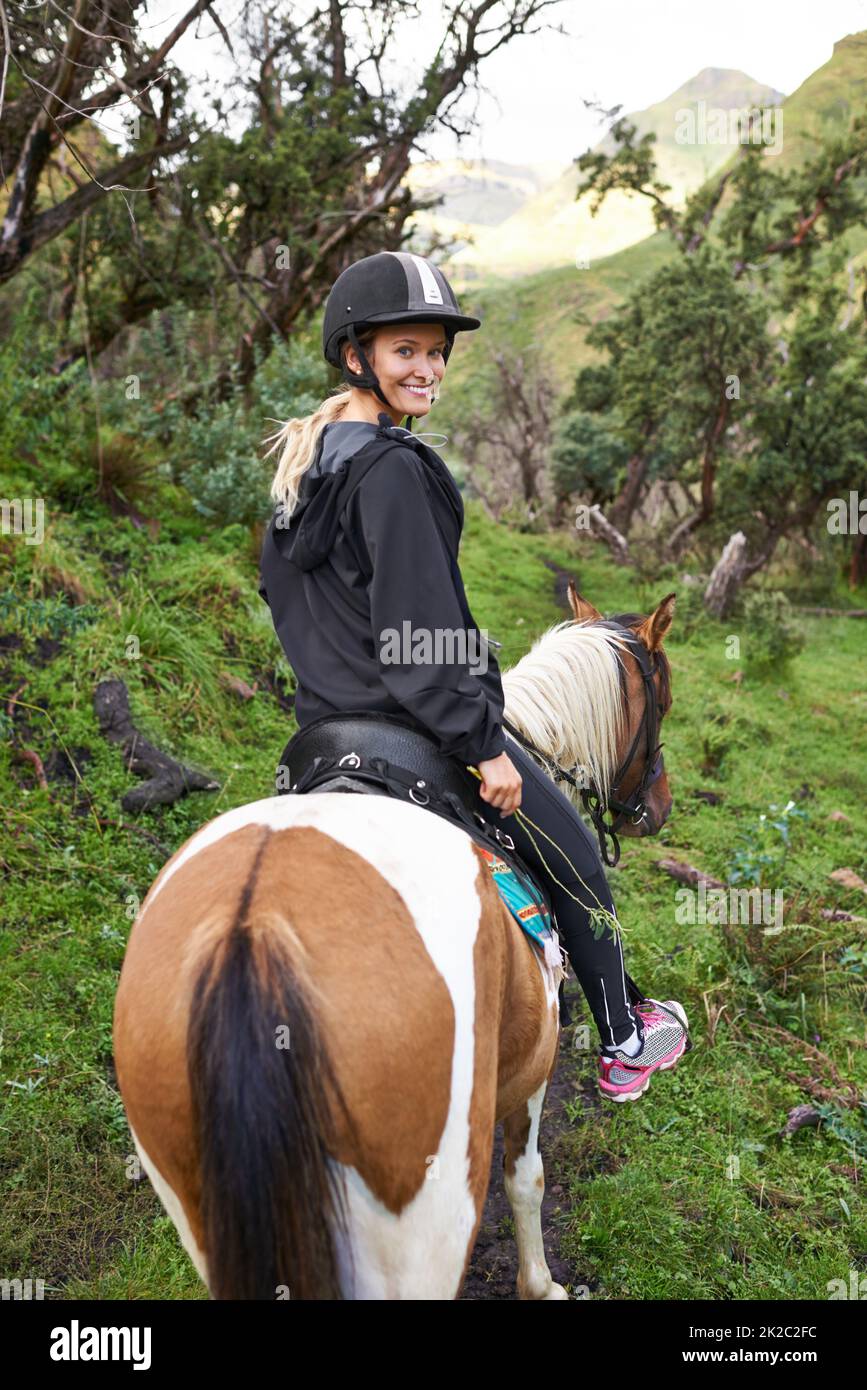 Horse riding in the outback. An attractive young woman riding a horse on a mountain trail. Stock Photo