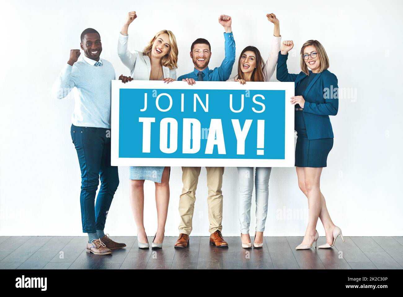 We want you on our team. Studio shot of businesspeople holding up a sign with the words join us today on it and cheering. Stock Photo