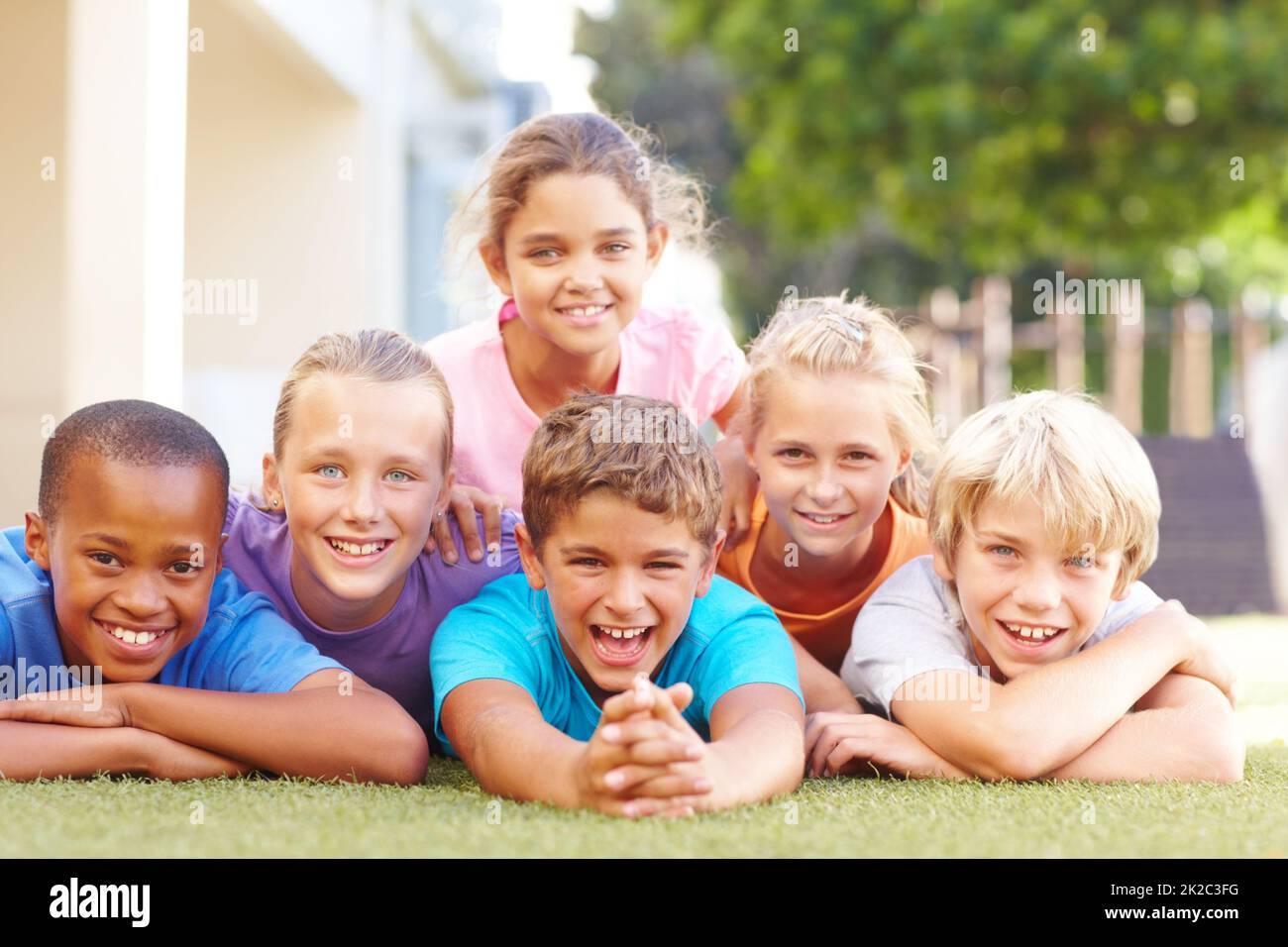 We love having fun together after school. Group portrait of happy school kids lying in a pile outside in the sun. Stock Photo