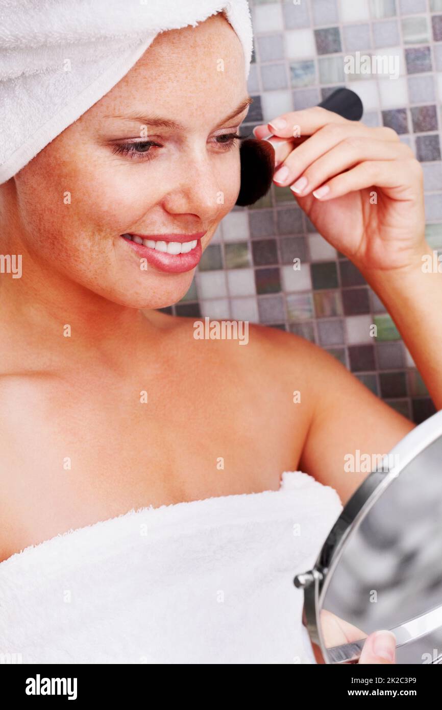 Happy female applying make up and using a hand mirror. Smiling young woman applying facial makeup and using a hand mirror. Stock Photo