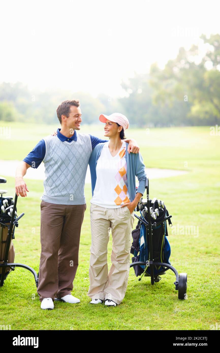 Happy couple on golf course. Full length of happy golfing couple with arms around smiling and looking at each other. Stock Photo