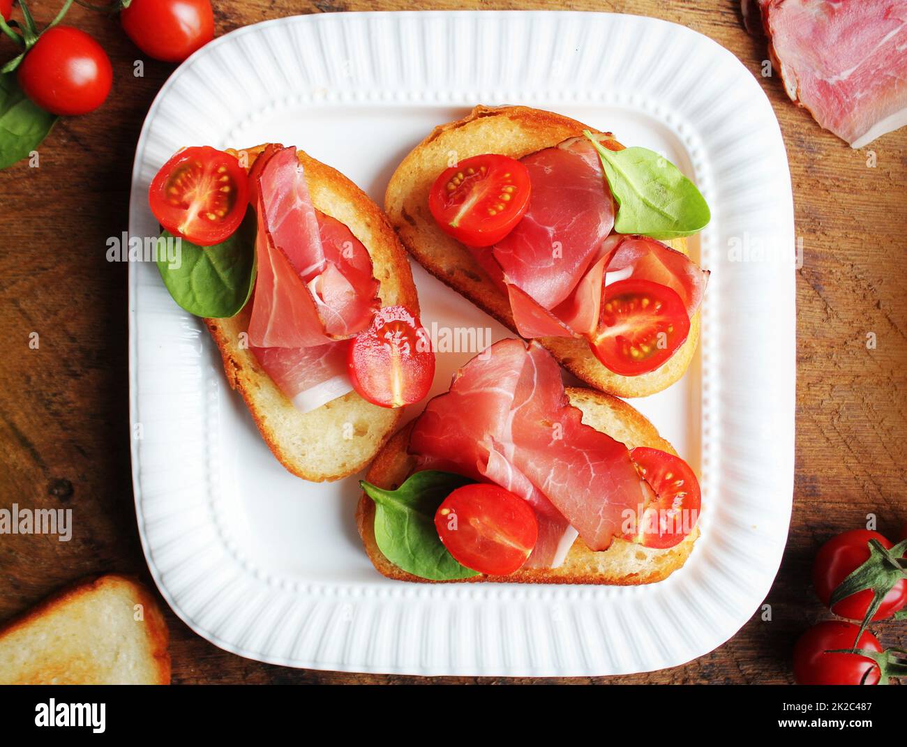 Bruschetta with prosciutto ham, cherry tomatoes and green spinach . Top view Stock Photo