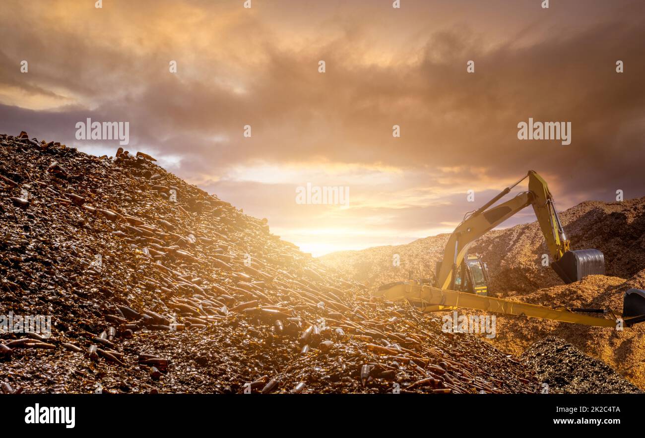 Blur photo of pile of brown glass bottle for recycle and backhoe on wood chips pile. Recycle materials. Paper industry. Glass bottle waste for recycle. Sustainable resources. Bulldozer working. Stock Photo