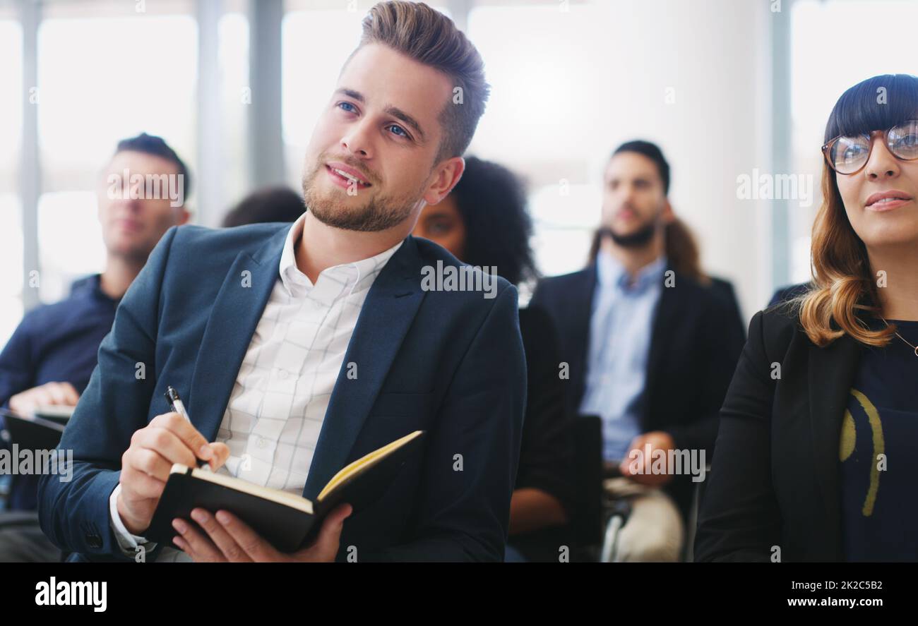 Eager to hear about this new brand on the market. Shot of a young businessman taking down notes while sitting in the audience of a business conference. Stock Photo