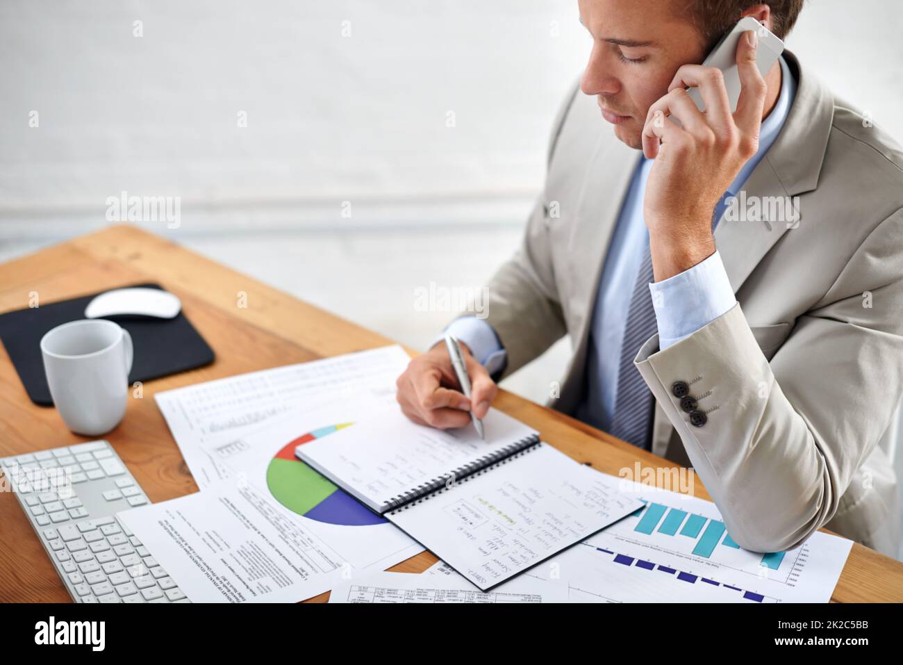 Your investments are safe with him. Shot of a young businessman talking on the phone while writing at his desk. Stock Photo