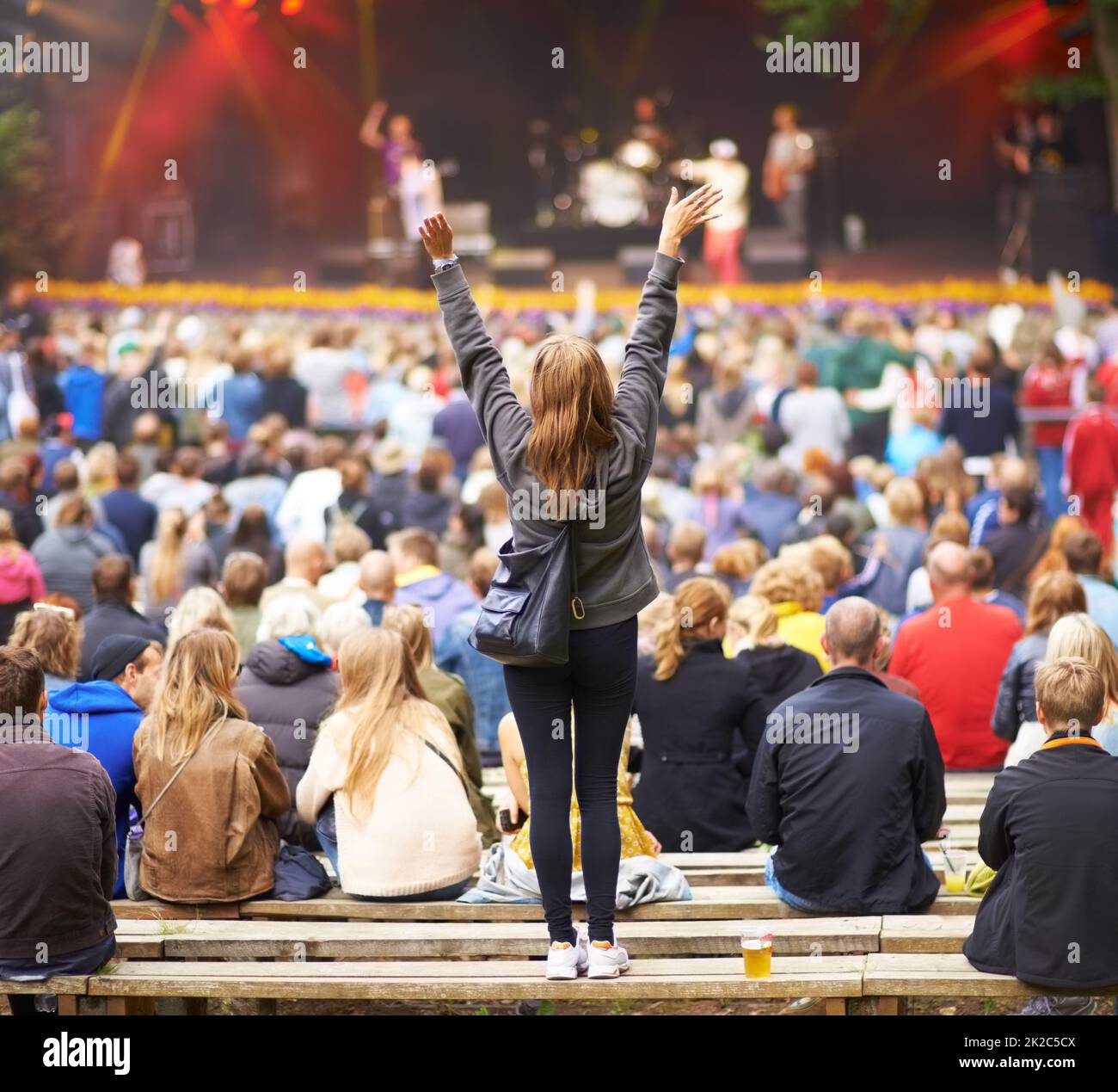 Guess whos her favourite band.... Rear-view shot of a crowd at an outdoor music festival with the focus on a female fan cheering. Stock Photo