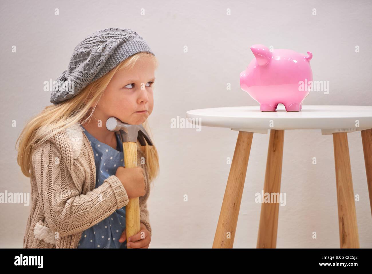 To break or not to break. A cute girl with a hammer eyeing her piggy bank. Stock Photo
