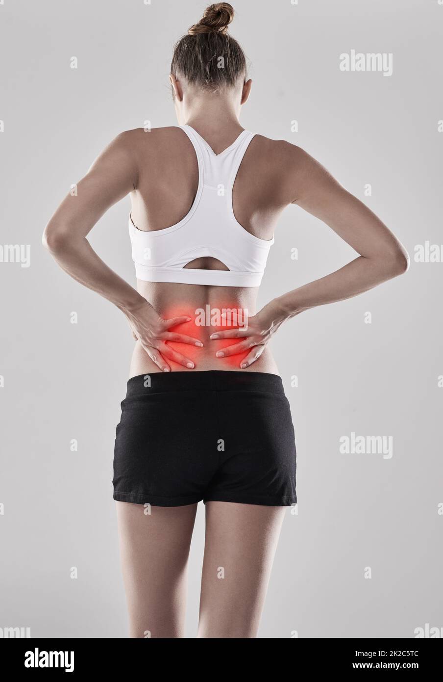 Pain in the back can be really unbearable and unpleasant. Shot of a young woman holding her injured back thats highlighted in red. Stock Photo