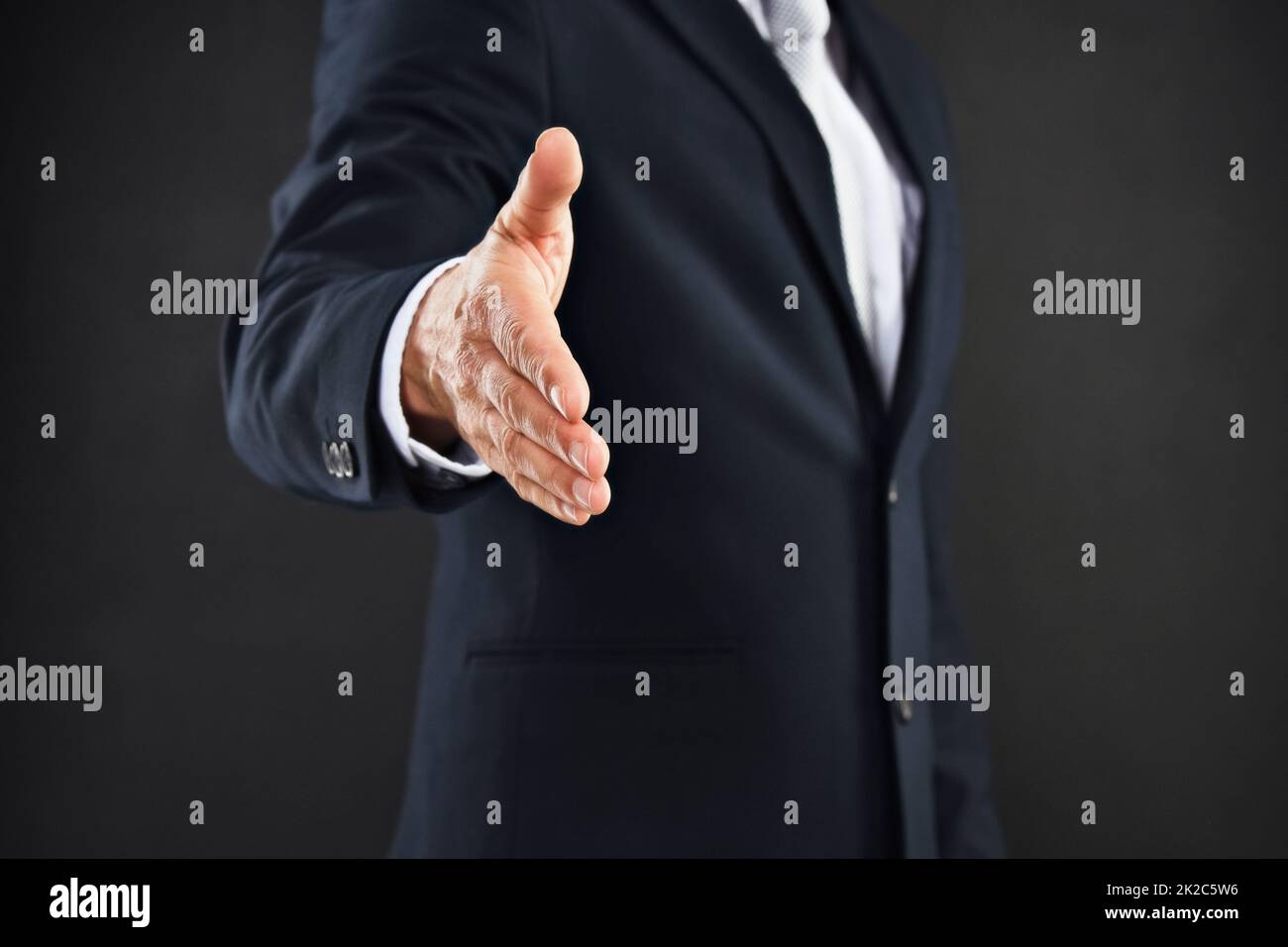 Lets do business. Cropped shot of a businessman extending his arm to shake hands against a black background. Stock Photo