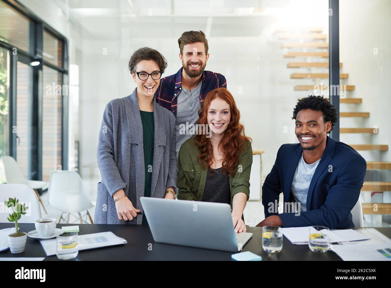 Were moving the company head-on towards success. Portrait of a group of young creatives working together on a laptop in a modern office. Stock Photo