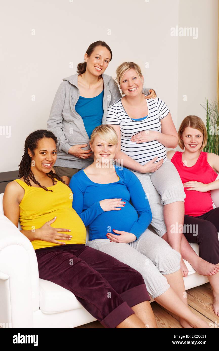 We cant wait for the big day. A group of multi-ethnic pregnant women sitting on a couch and smiling at the camera. Stock Photo