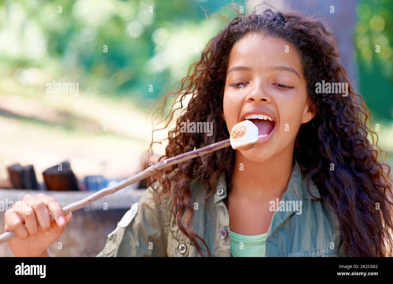 Biting into deliciousness. A young girl biting a fireside treat. Stock Photo