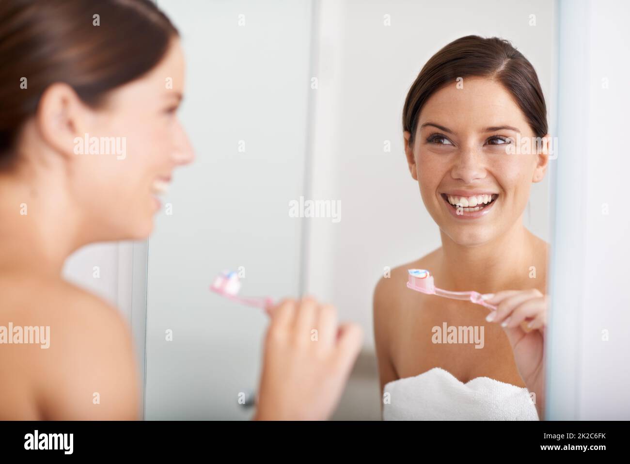 Dental health is important. A young woman standing in front of the mirror brushing her teeth. Stock Photo