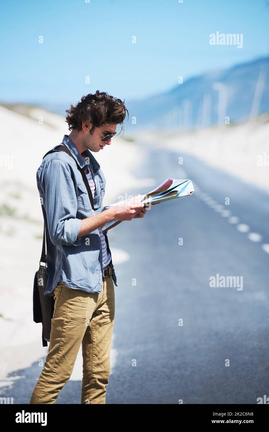 Trying to map out my journey. Young man standing on the side of the road reading a map. Stock Photo