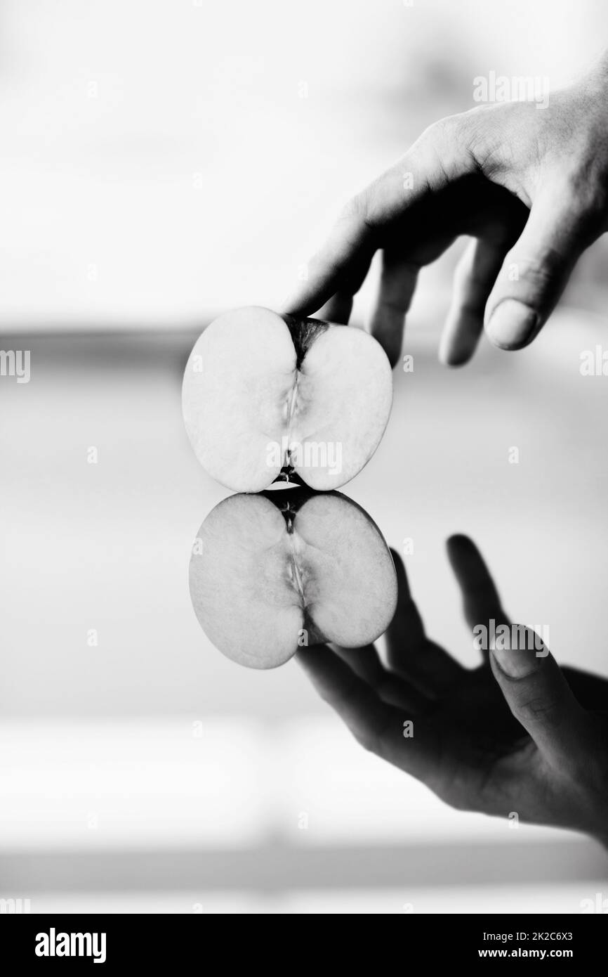 Reflecting on health. A hand holding half an apple against a shiny surface with its reflection underneath. Stock Photo