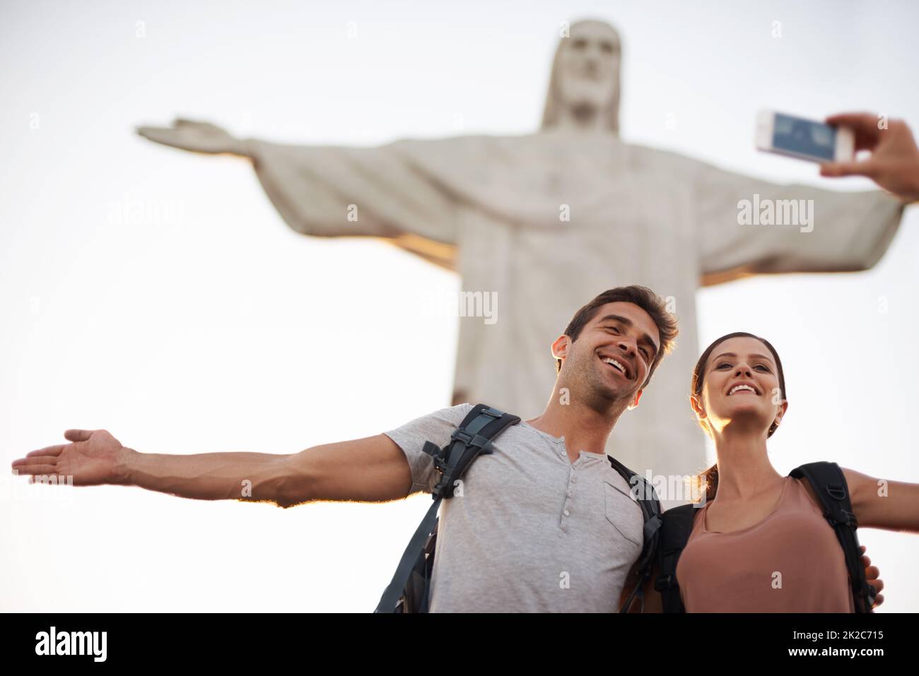 Take one while we pose. Shot of a happy young couple taking photos at the Christ the Redeemer statue. Stock Photo