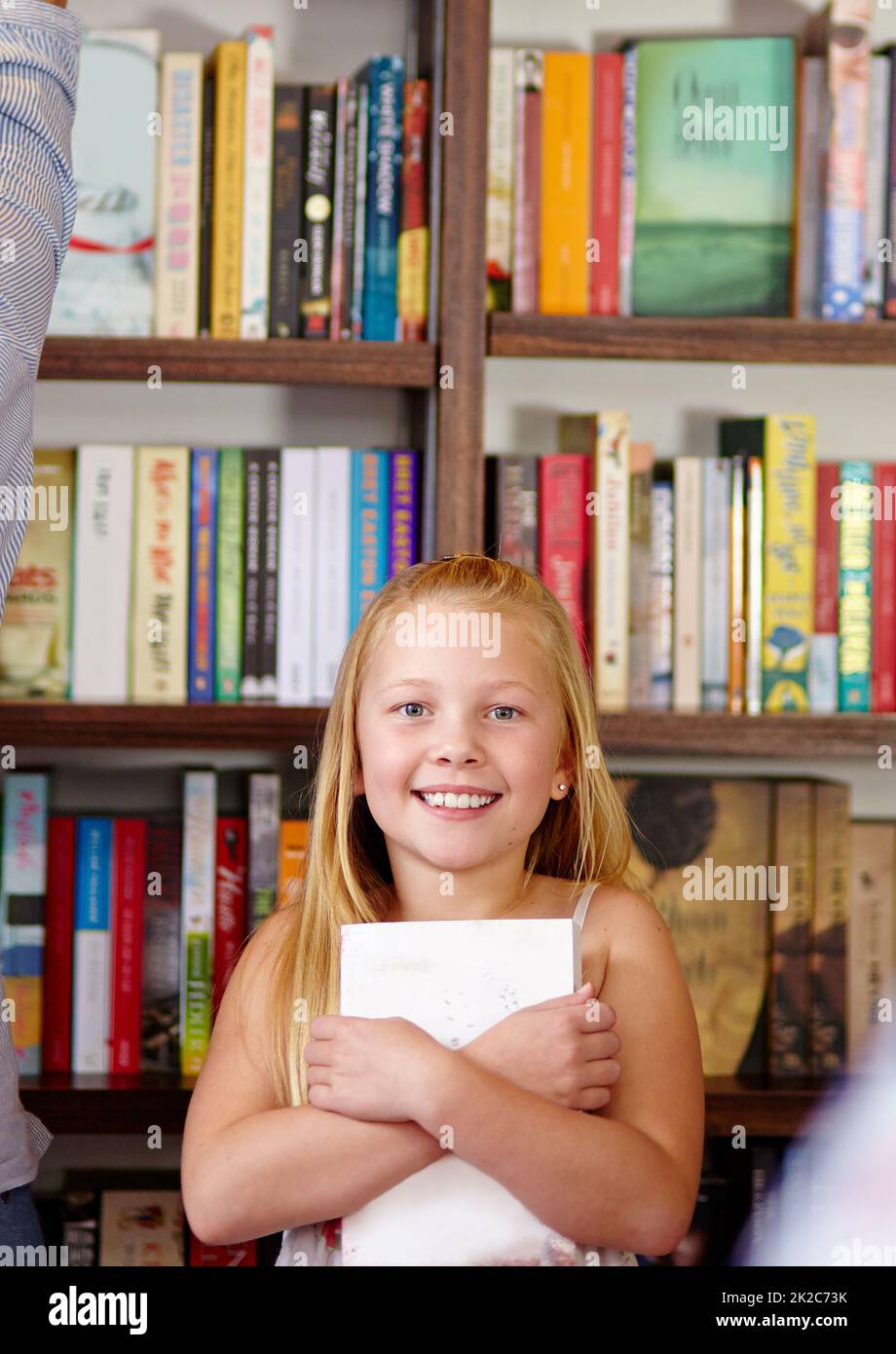 I love books. A cute young girl clutching her book in a library. Stock Photo
