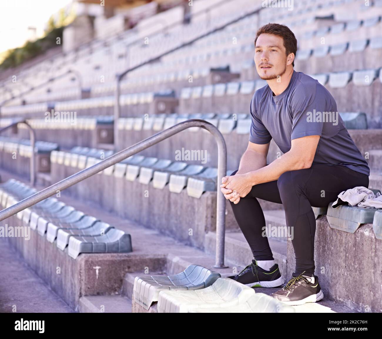 Taking it all in. Shot of a handsome young man sitting in the stands at an athletics arena. Stock Photo