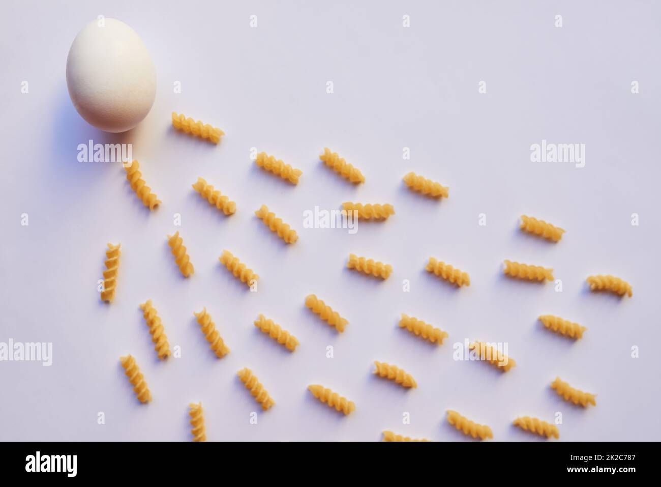 How life gets created. Studio shot of an egg against a grey background while being surrounded by lots of little pieces of pasta. Stock Photo