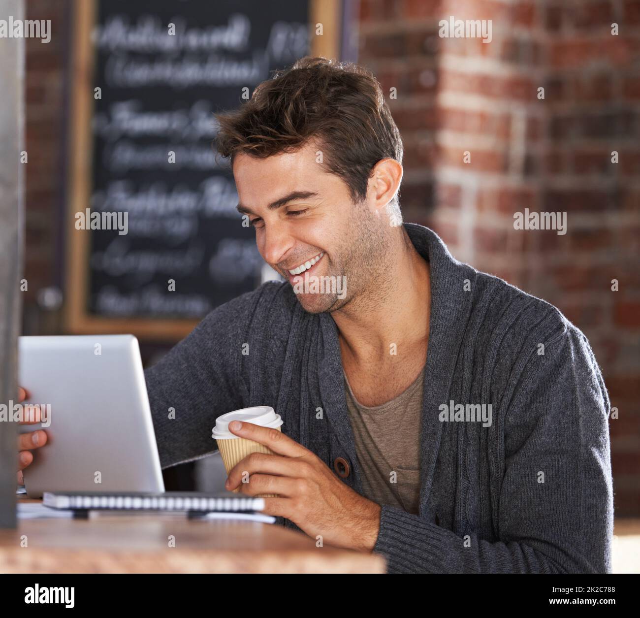 Great wifi and good coffee. A young man working on a digital tablet holding a coffee in a restaurant. Stock Photo