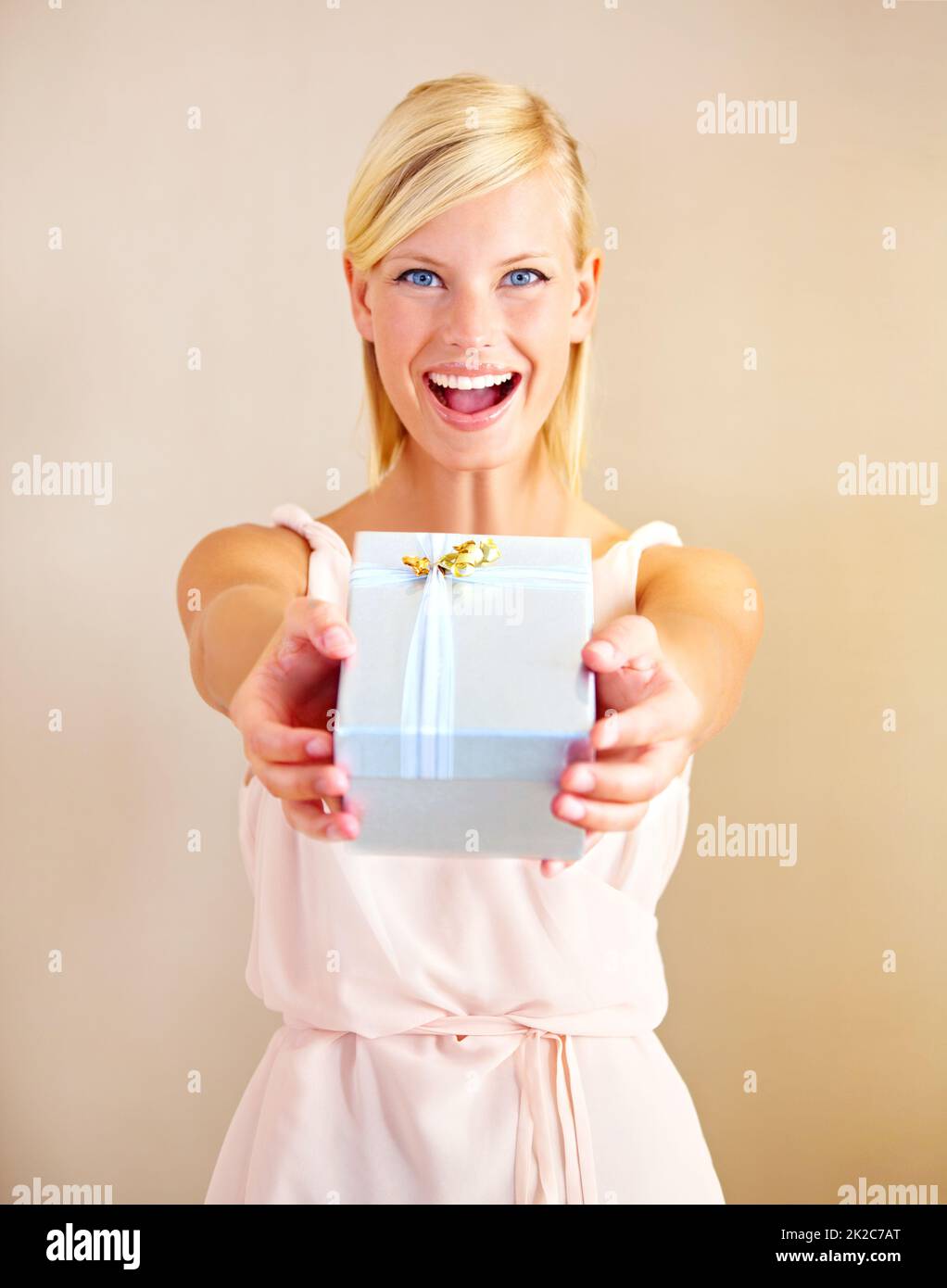 Surprise - its for you. Portrait of a young woman holding out a gift box and smiling. Stock Photo