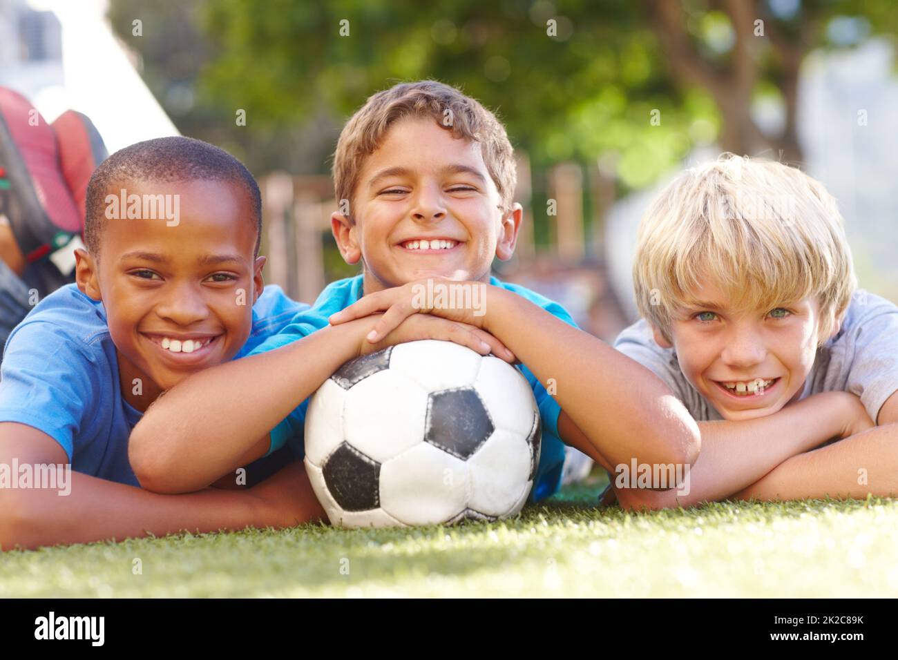 A winning team of best friends. Three happy boys lying outside in the sun with their soccerball - copyspace. Stock Photo
