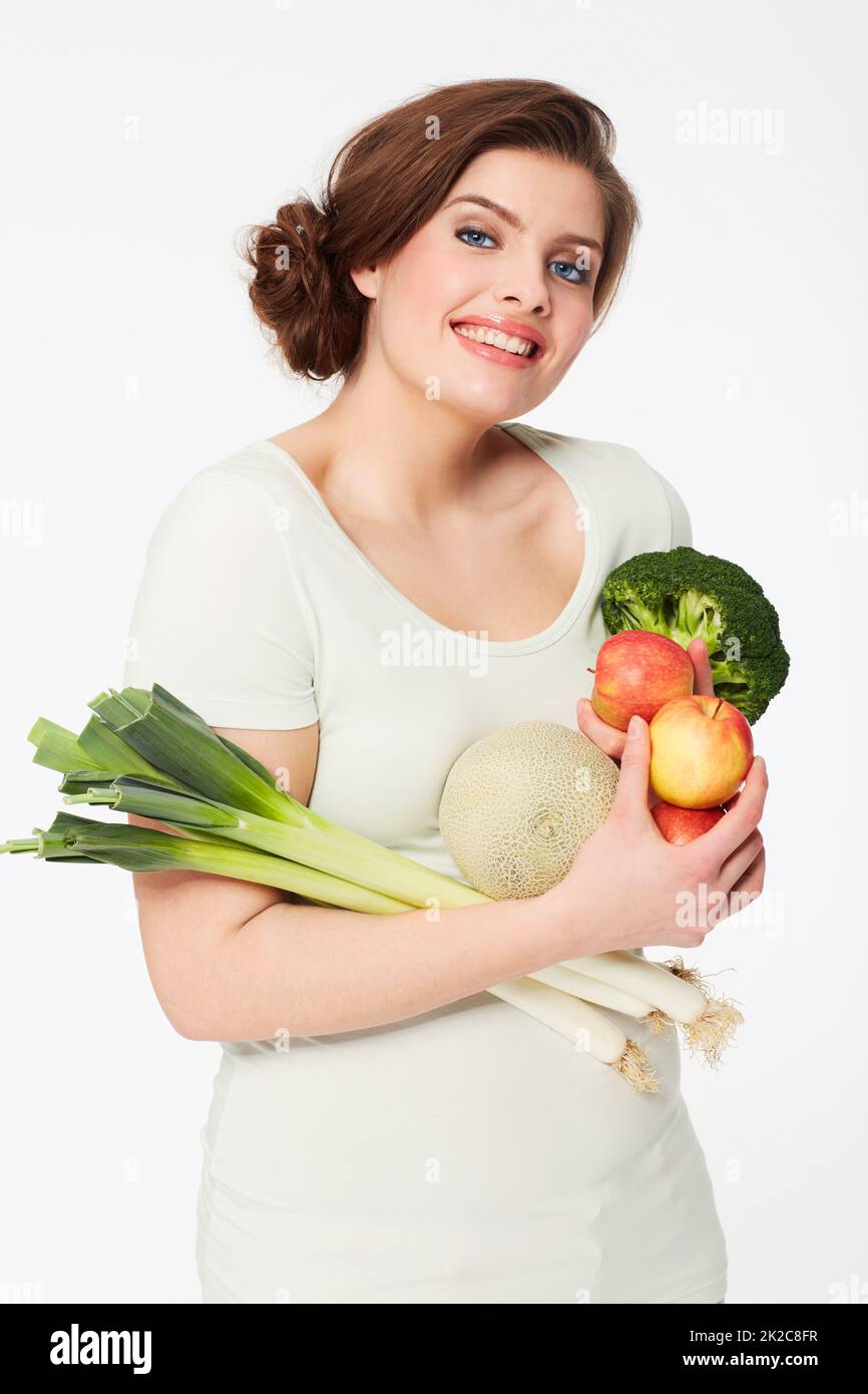 Healthy on the inside, happy on the outside. Pretty brunette woman holding healthy veggies while isolated on white. Stock Photo