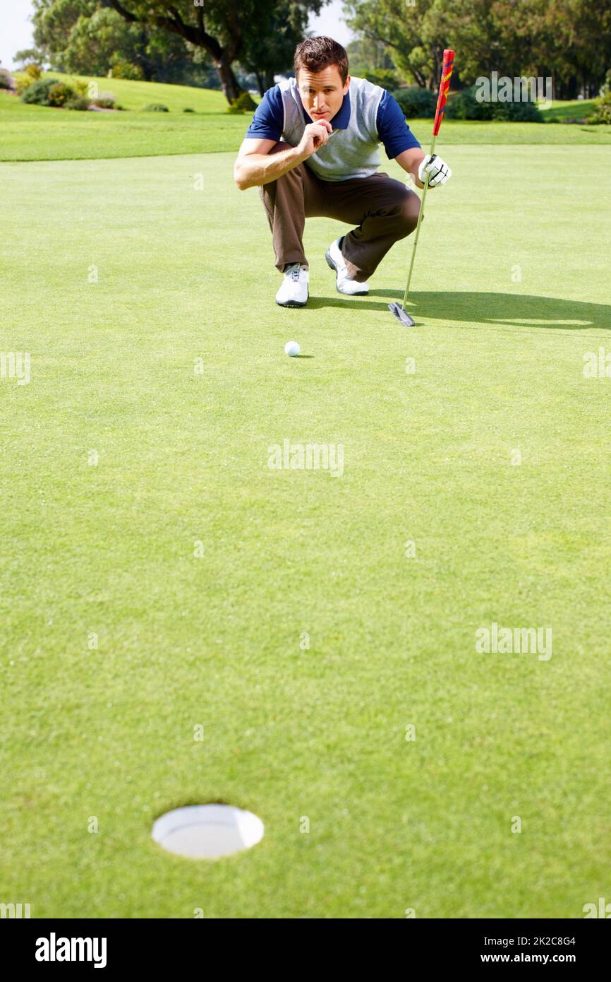 Man assessing his options to putt. Full length of man crouching on the putting green and assessing his options to putt the ball. Stock Photo