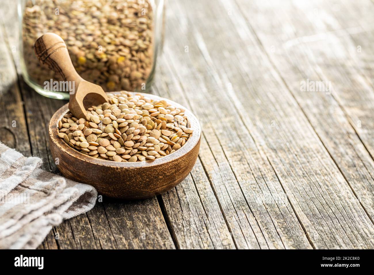 Uncooked brown lentils. Raw legume in bowl on wooden table. Stock Photo