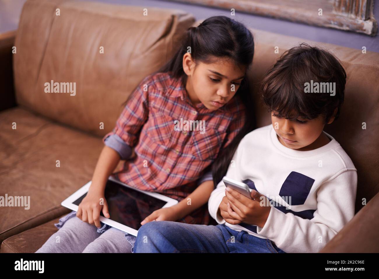Playing around with tech. Shot of two siblings playing with their digital devices at home. Stock Photo