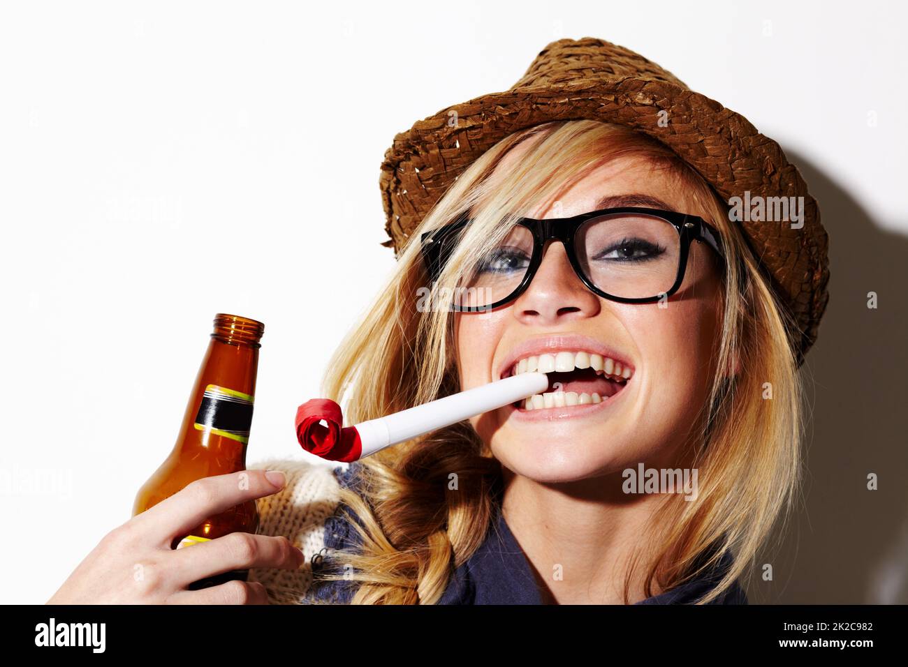 Youre never too old to enjoy party favors. A gorgeous young woman with a party favor in her mouth holding a beer. Stock Photo