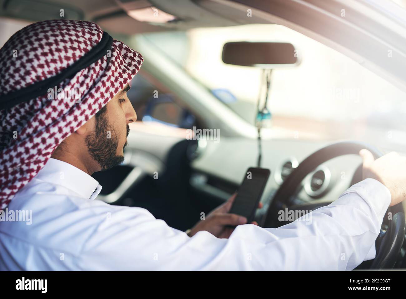 You have reached your destination. Shot of a young muslim businessman using his phone while driving a car. Stock Photo