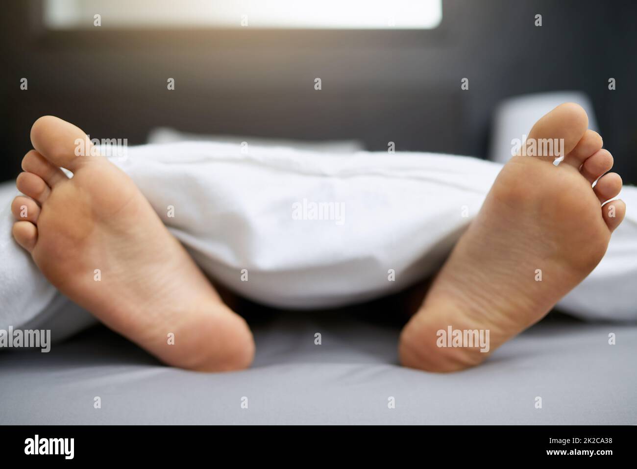 Do not disturb. Shot of a young mans feet sticking out from underneath his duvet. Stock Photo