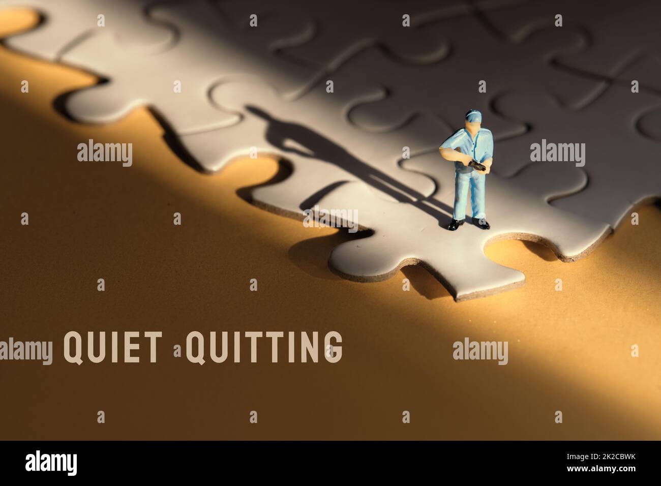 Concept of quiet quitting, job burnout, depression. Single tiny worker miniature figure on edge of linked blue jigsaw puzzle. Yellow paper background Stock Photo