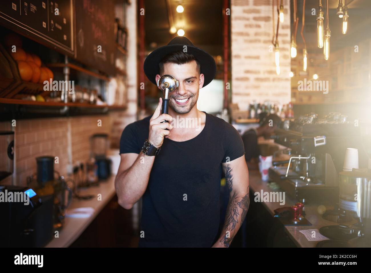 We like to keep it fun around here. Shot of a young man covering his eye with a coffee filter while working in a cafe. Stock Photo