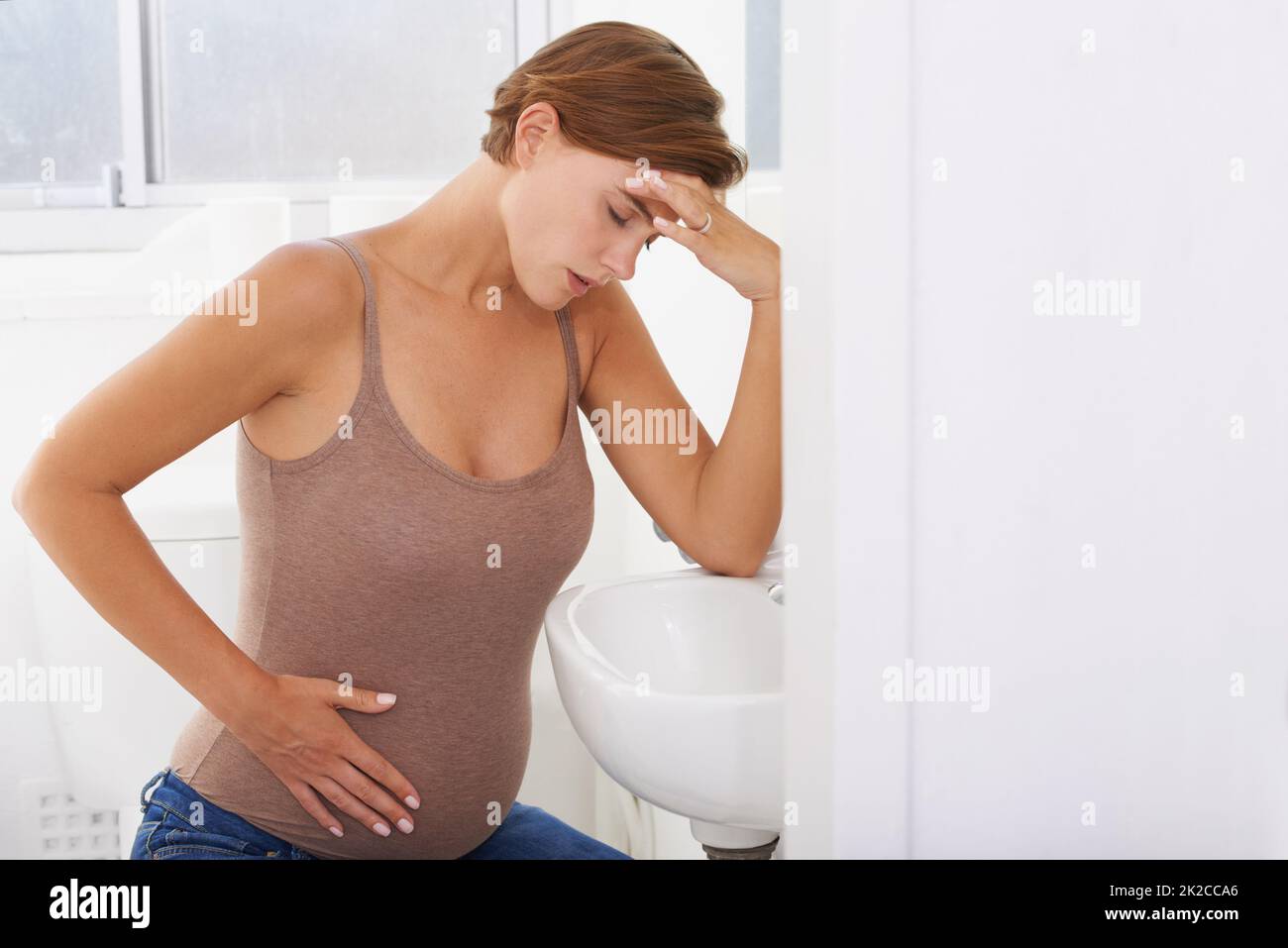 The aches and pains of pregnancy. A pregnant woman struggling with morning sickness in the bathroom. Stock Photo