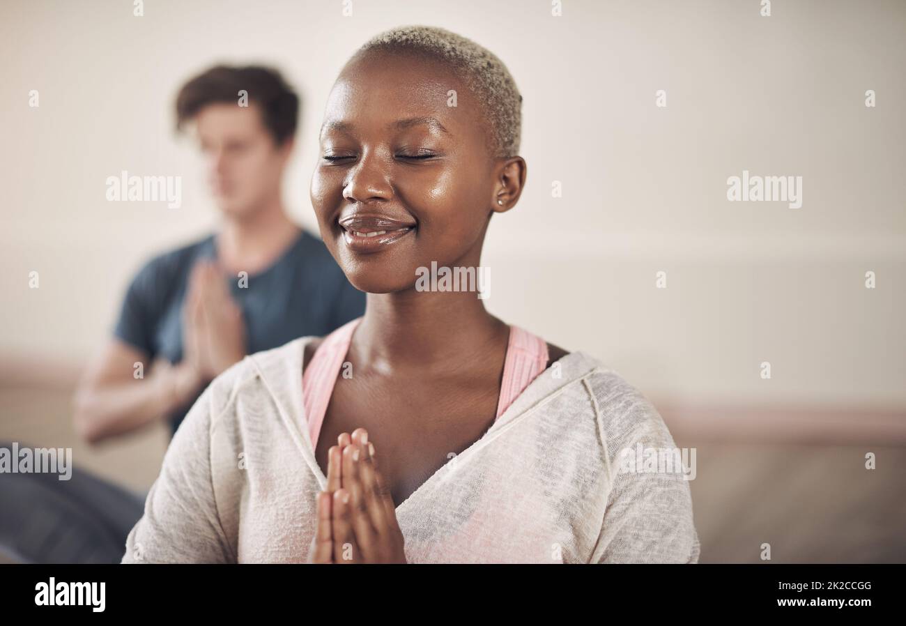 Meditation is both the means and the end. Cropped shot of an attractive young woman sitting and meditating after a yoga class indoors. Stock Photo