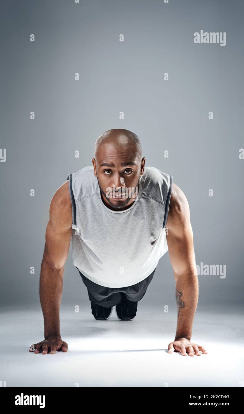 Push yourself when everyone else is knocking you down. Shot of a sporty young man doing push ups against a grey background. Stock Photo