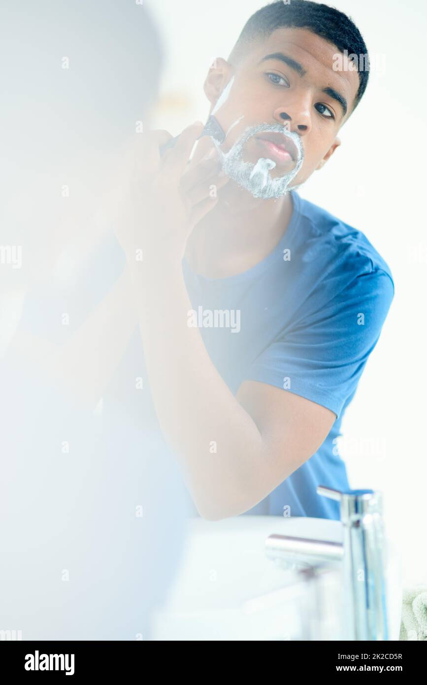Time to shave this all off. Shot of young man shaving his face in his bathroom mirror. Stock Photo